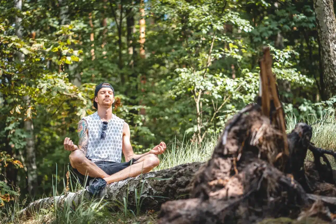A man meditation in the forest while sitting on a fallen tree log