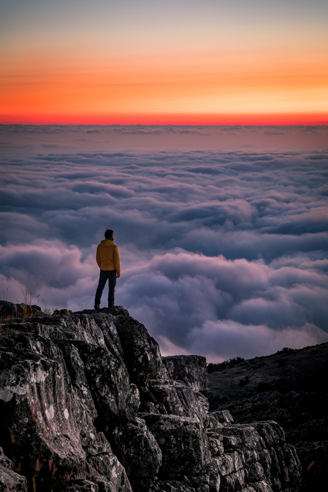 Man stands on a mountain watching the sunset.