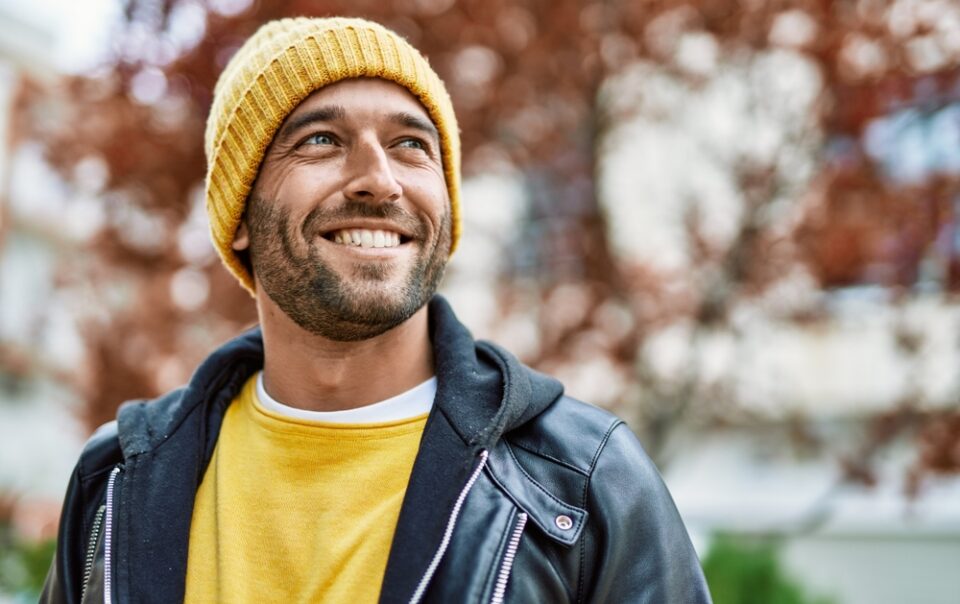 A man smiles while standing outside.