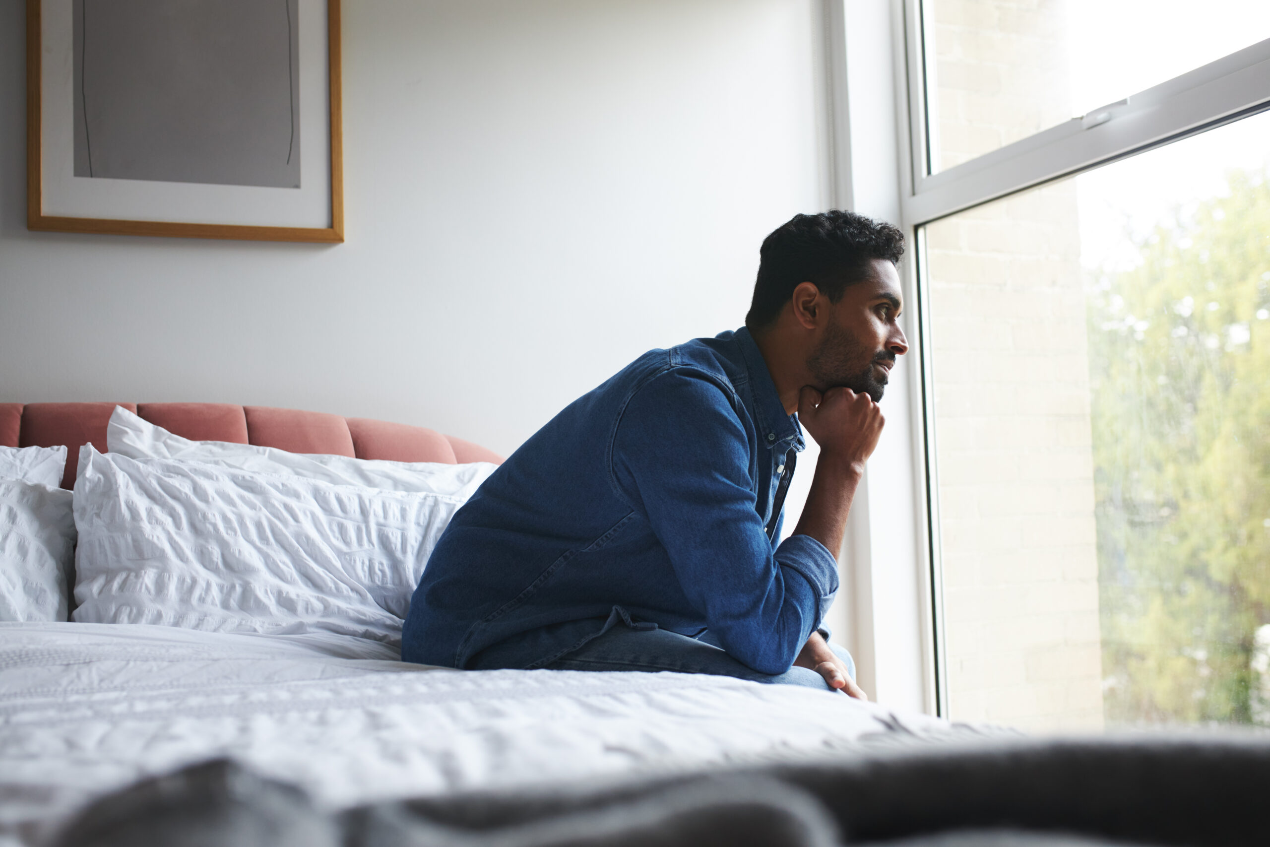 A man in a 30-day rehab program sitting on a bed looking happy and thoughtful.