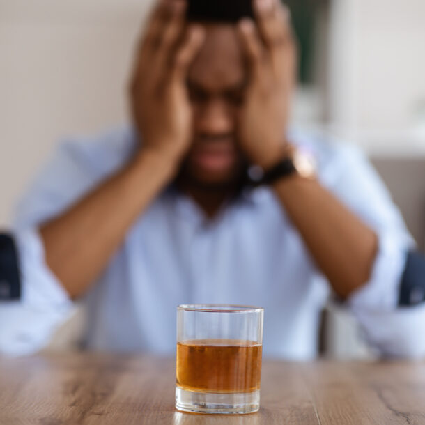 A man sitting his his hands on his head in front of a glass of alcohol wondering am i addicted to alcohol.