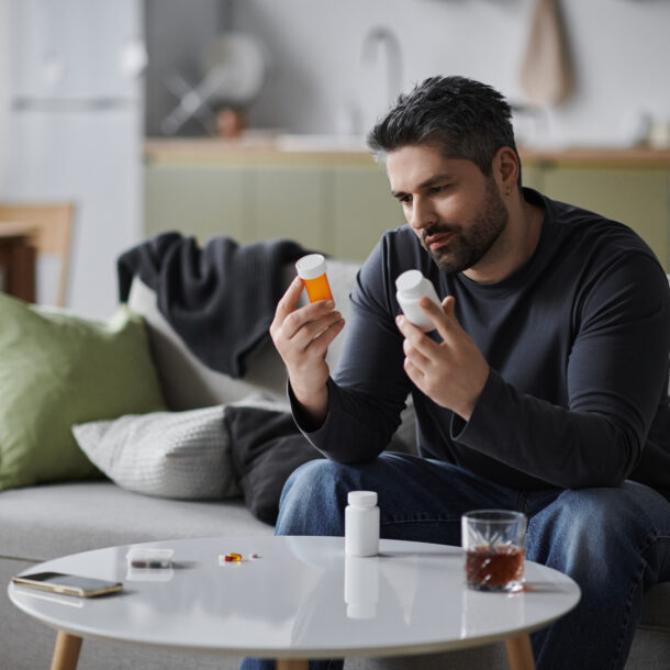 A man sitting on a couch holding bottles of pills asking himself am i addicted to prescription drugs.