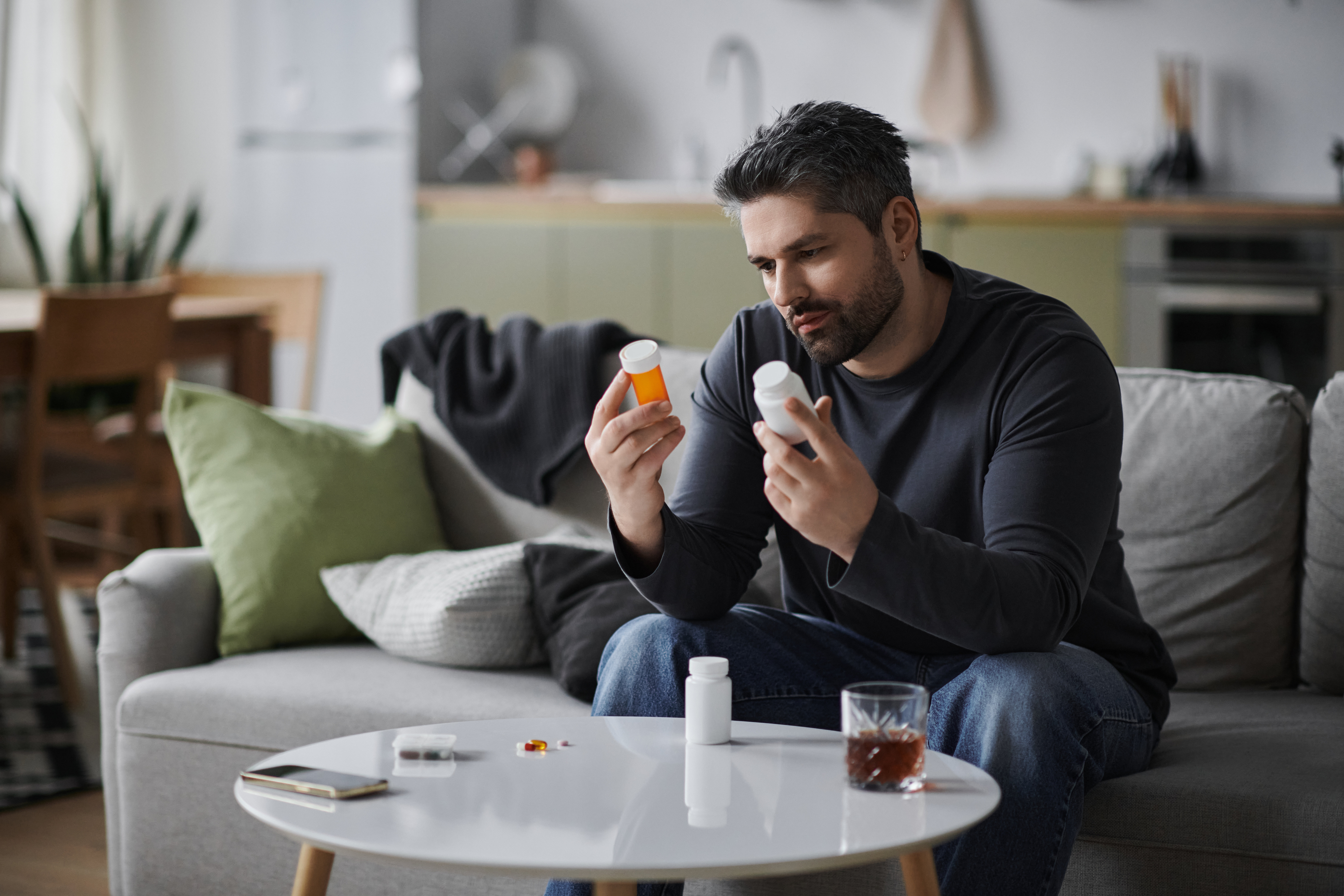 A man sitting on a couch holding bottles of pills asking himself am i addicted to prescription drugs.